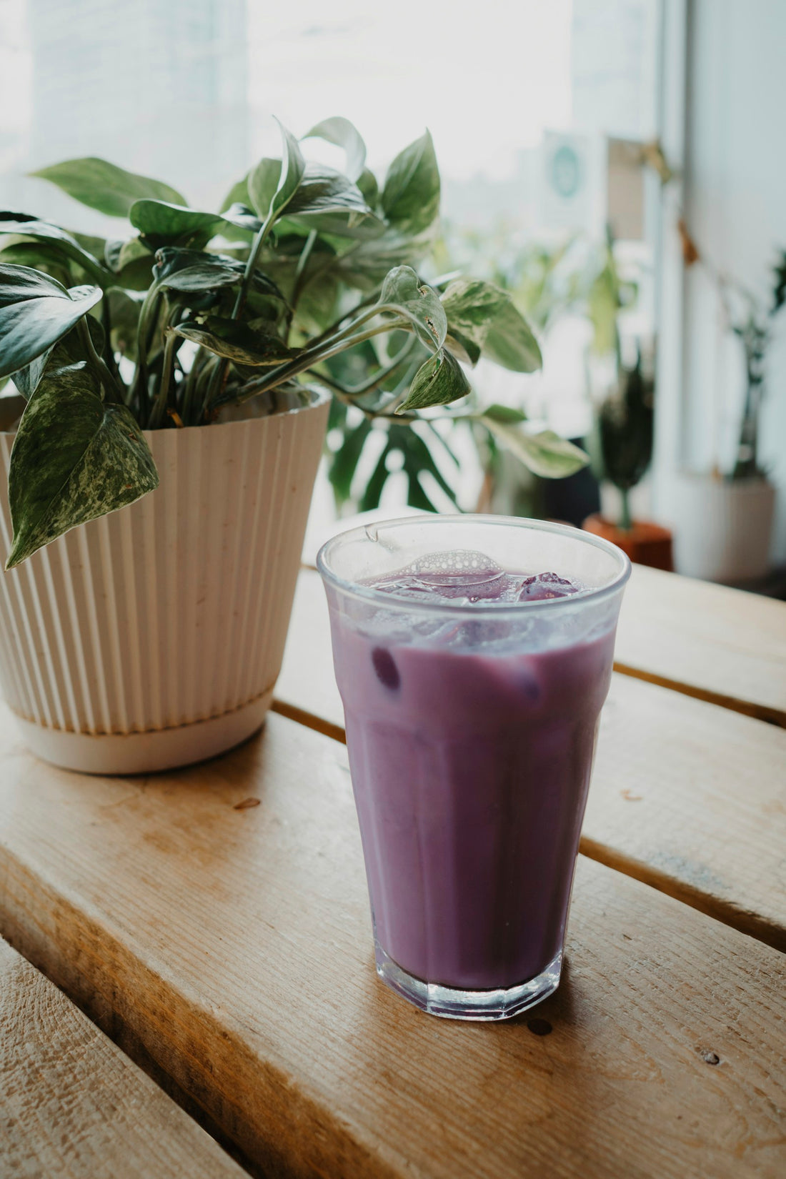 Ube latte glacé dans un verre, posé sur une table en bois à côté d'une plante